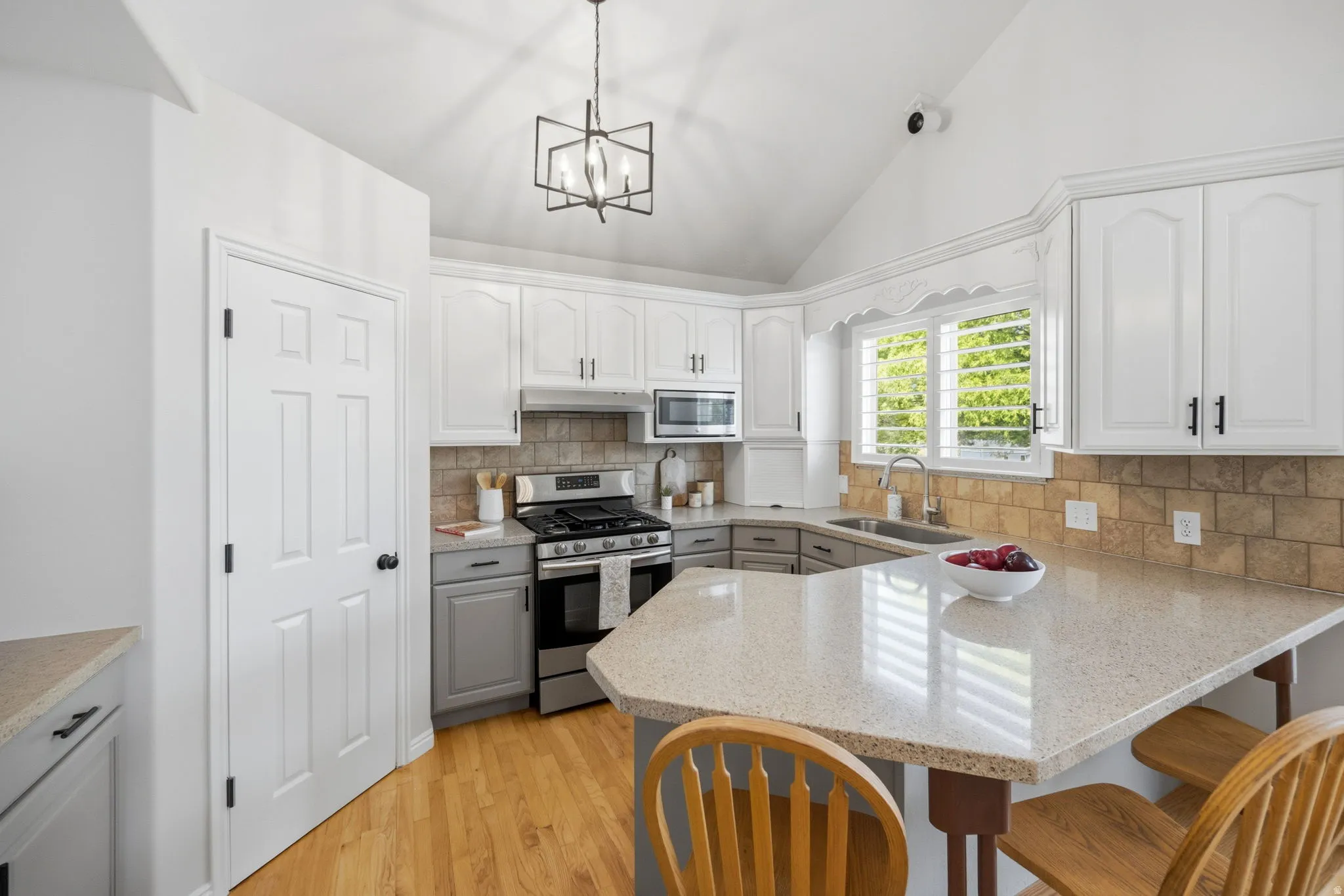 Kitchen featuring vaulted ceilings, wood-finish flooring, white upper cabinetry, gray lower cabinetry, and a light-toned countertop with an integrated breakfast bar