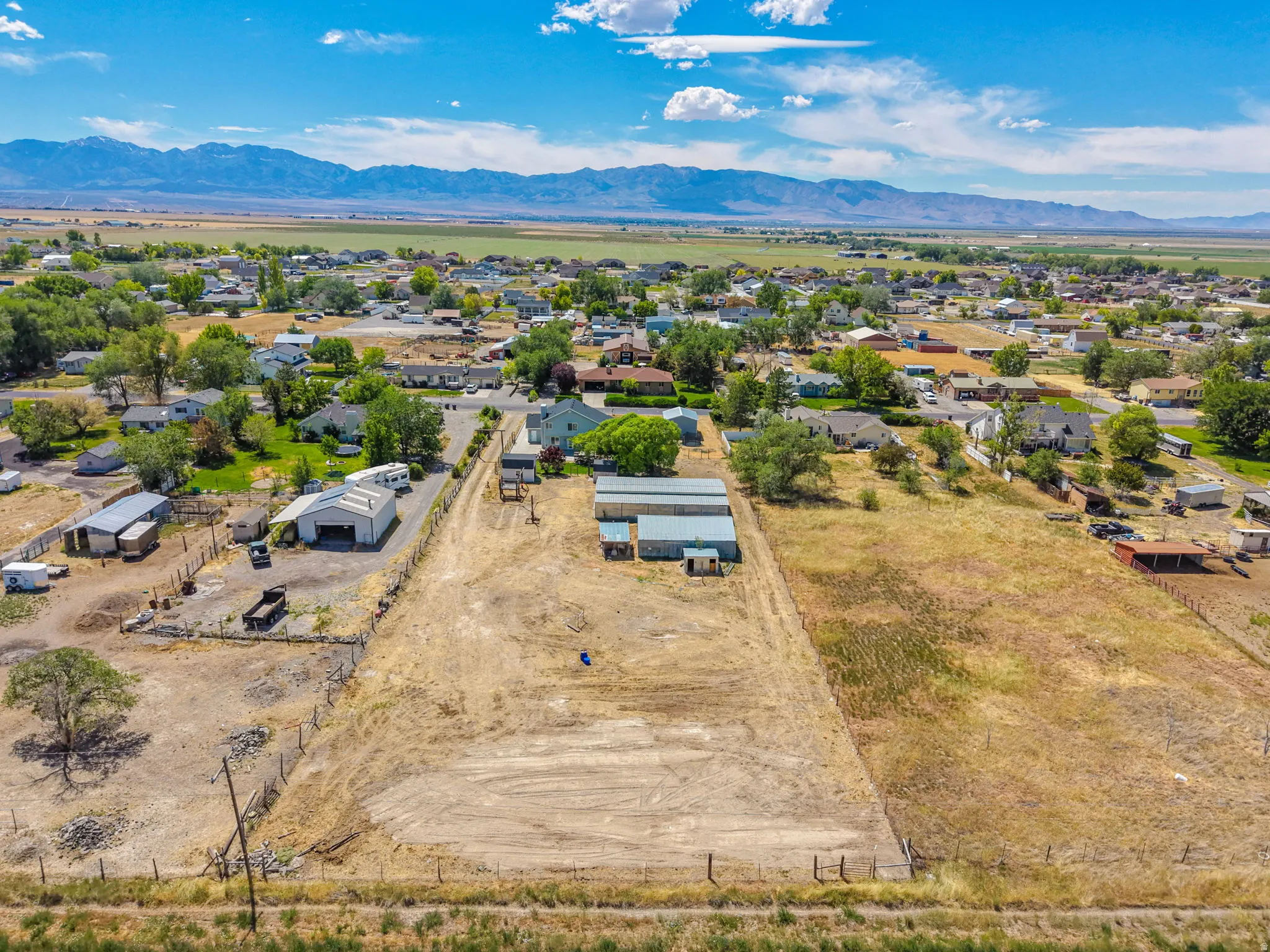 Expansive land parcel featuring existing structures, a partially fenced perimeter, and a gravel driveway