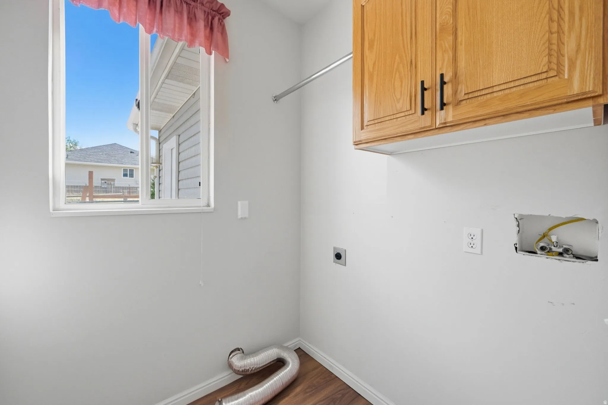 Laundry area featuring wood-finish flooring, built-in upper cabinetry with black hardware, and an overhead clothes hanging rod