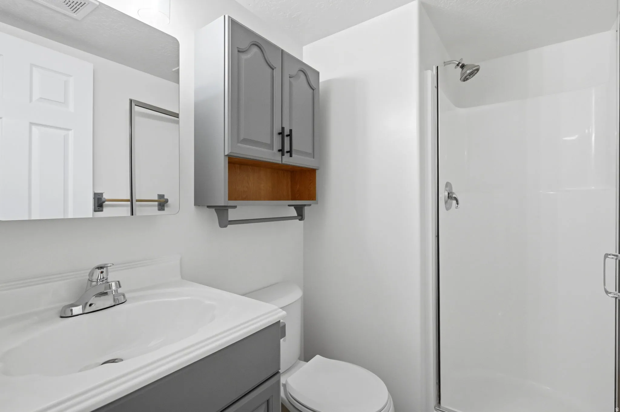 Bathroom featuring a white vanity with a chrome faucet, wall-mounted mirror, and a shower stall with a glass enclosure