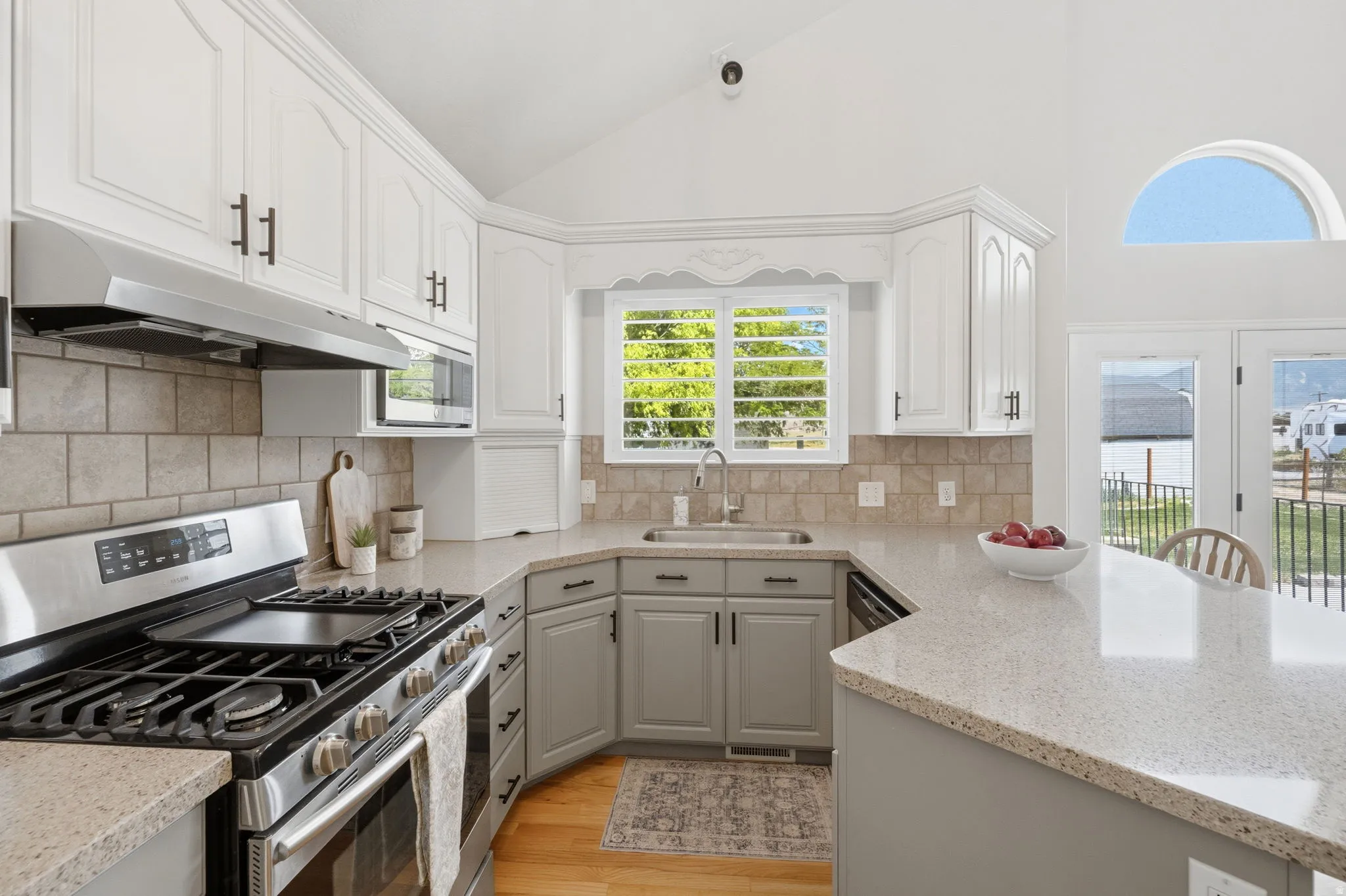 Vaulted ceiling kitchen featuring white upper cabinetry, gray lower cabinetry, and light-toned countertops