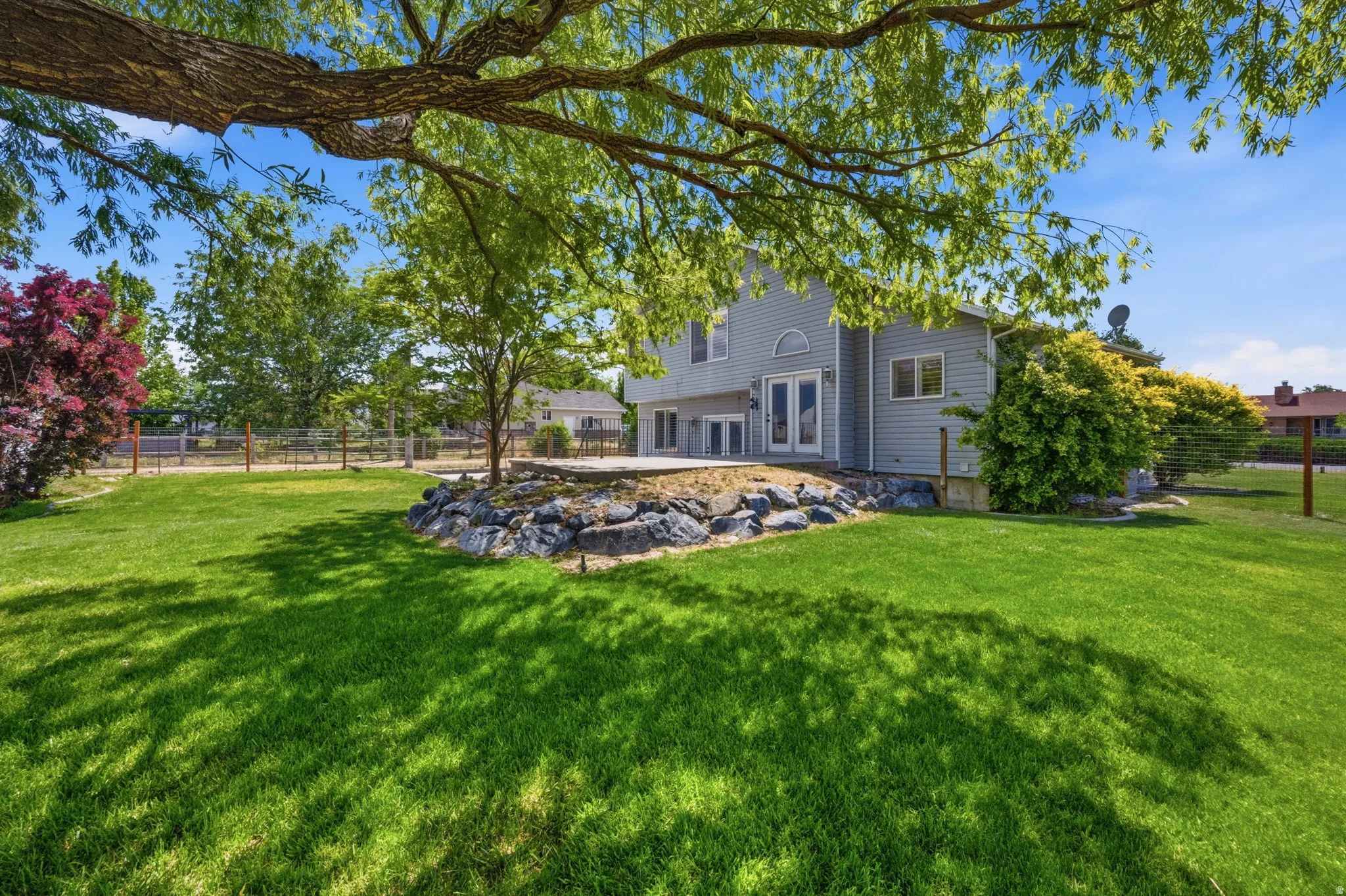Expansive green lawn with mature trees and a rock-lined planting area