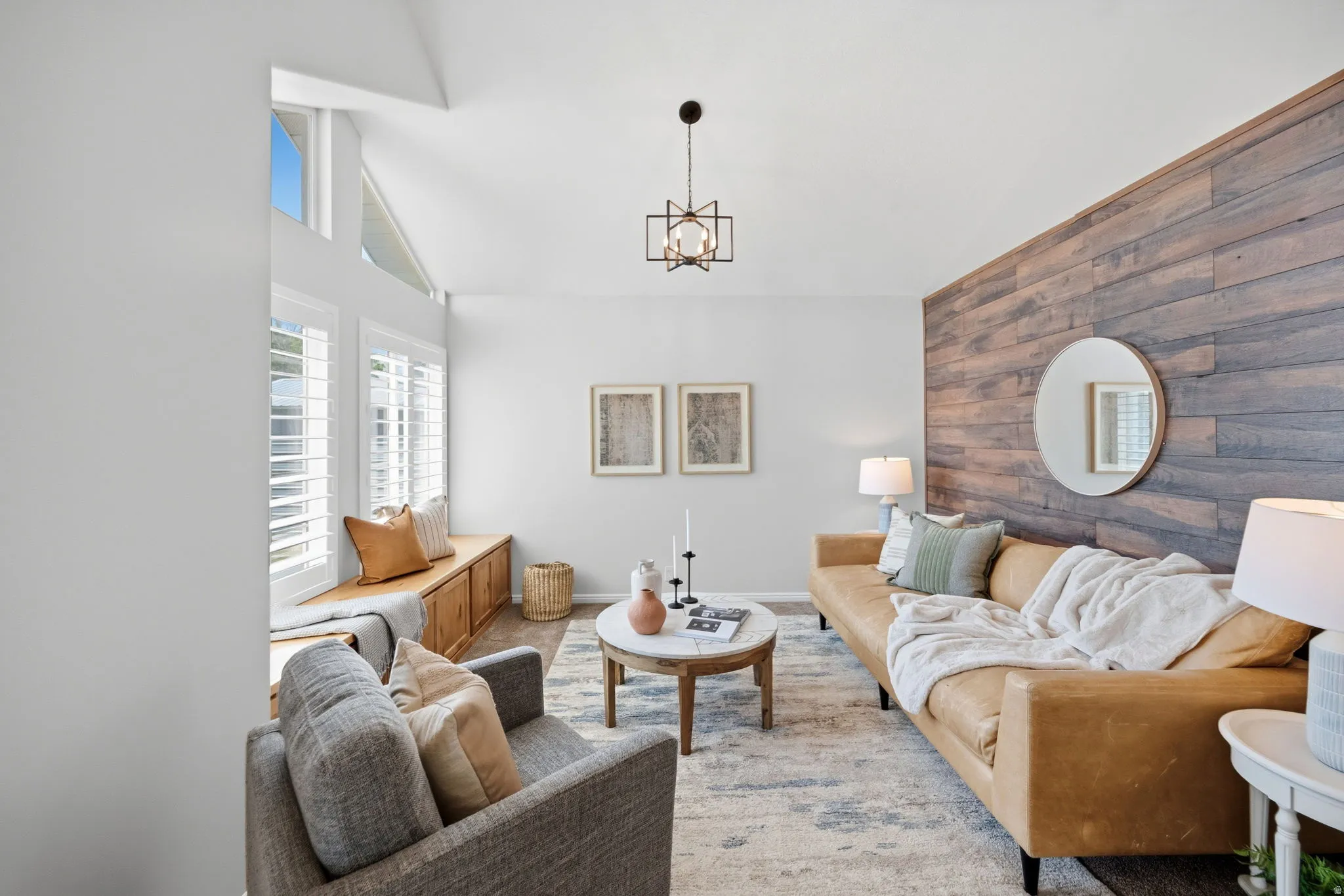 Vaulted ceiling featuring a contemporary chandelier, a built-in window seat with storage, white plantation shutters, a wood-paneled accent wall, and wood-finish flooring