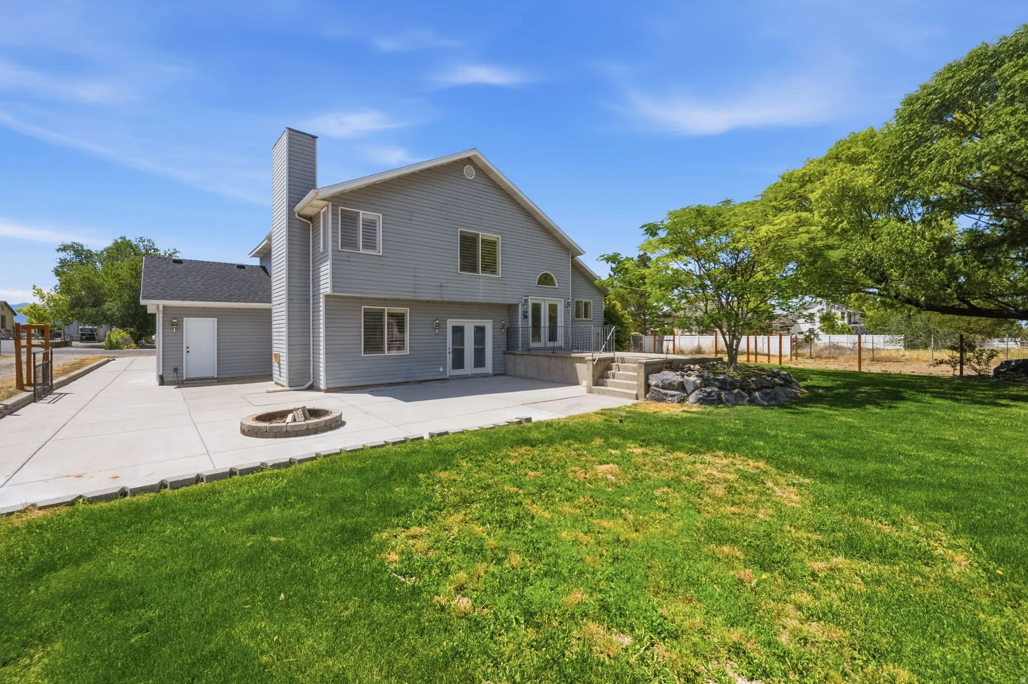Expansive backyard featuring a manicured lawn, concrete patio with a built-in fire pit, and mature trees