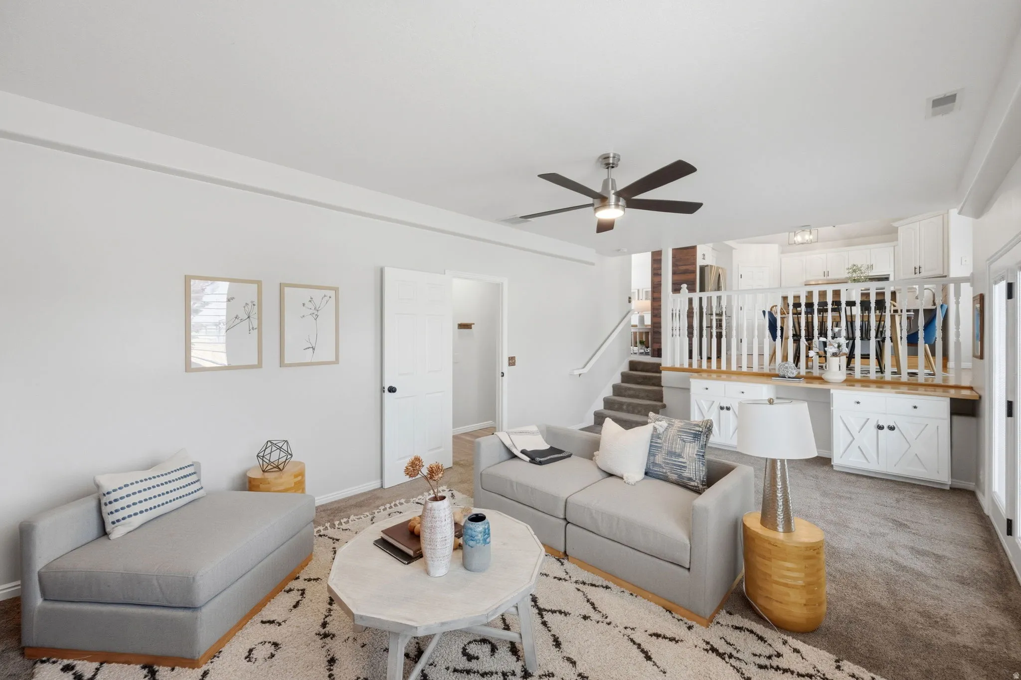 Open-concept living area featuring a ceiling fan, plush carpet flooring, and a stairway with carpeted treads