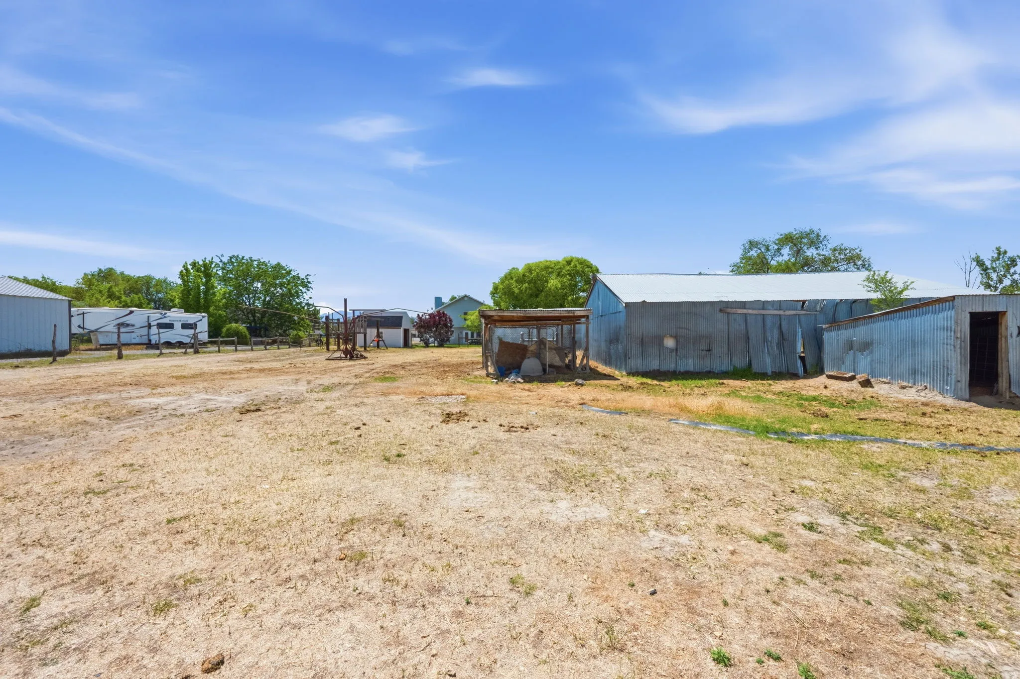 Expansive outdoor space featuring multiple outbuildings, including a large corrugated metal structure with a pitched roof and a smaller open-sided shed
