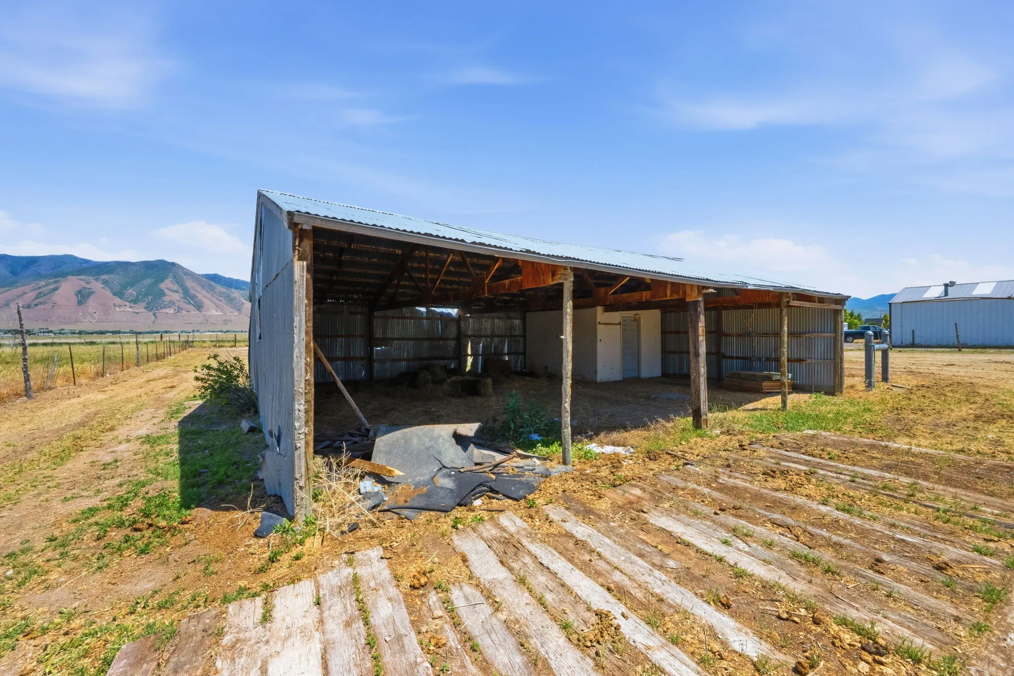 Open-sided barn structure featuring a corrugated metal roof and exposed wood beams