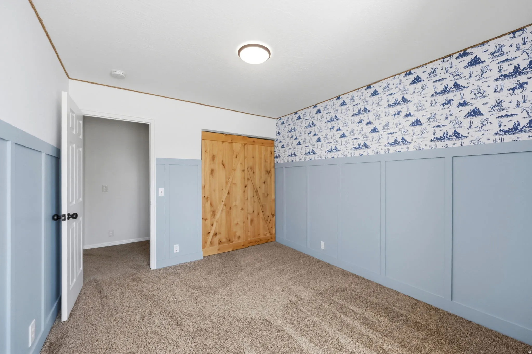 Spacious room featuring board and batten wainscoting, patterned wallpaper, and a natural wood-finish barn door