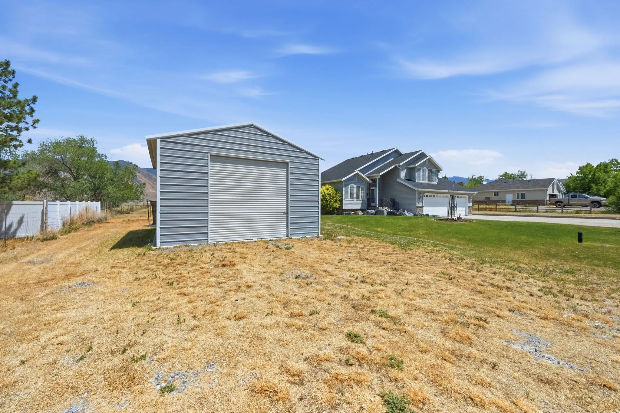Detached gray metal shed with roll-up garage door, set on a sloped lot