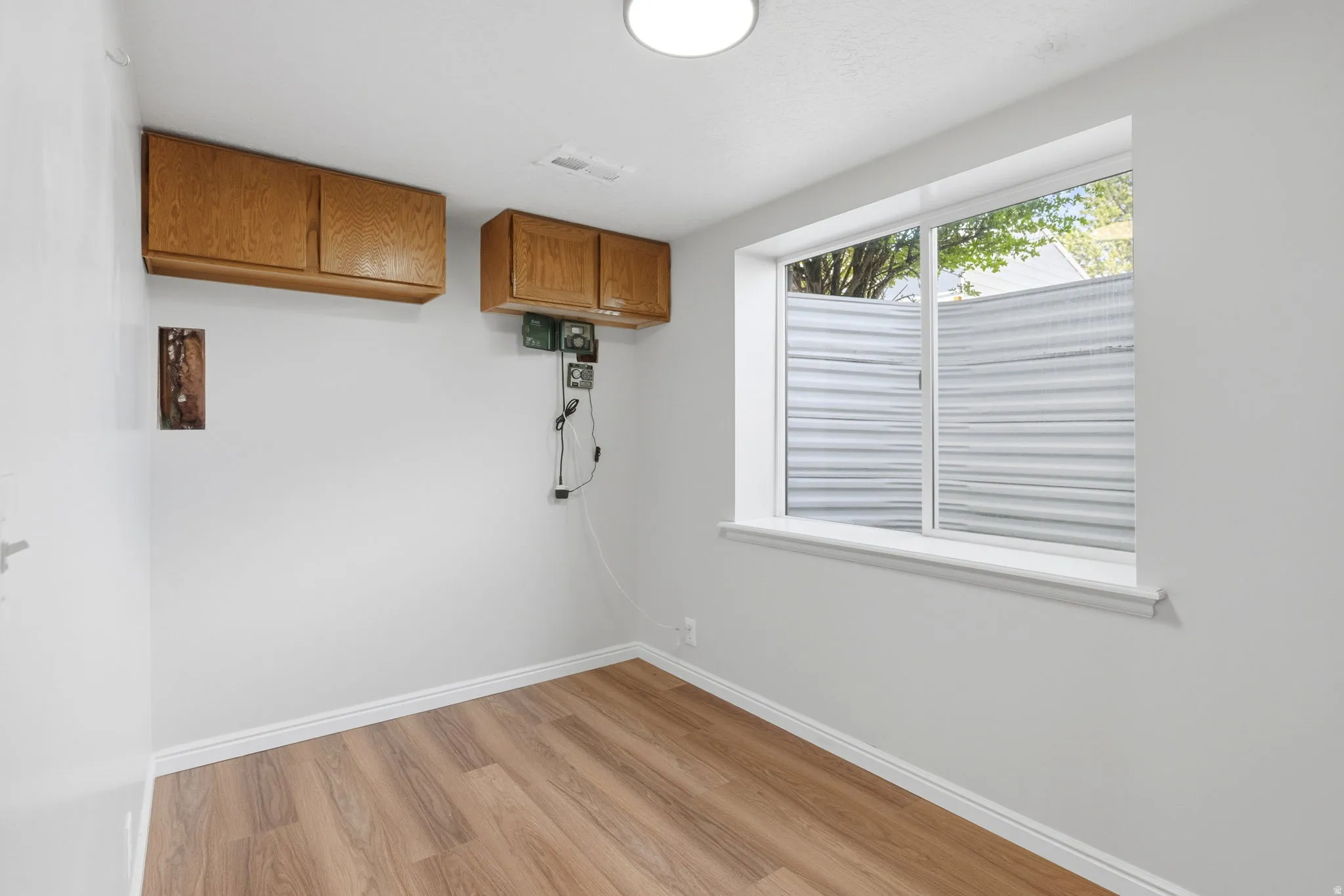 Room with wood-finish flooring, white walls, and a large window featuring horizontal blinds