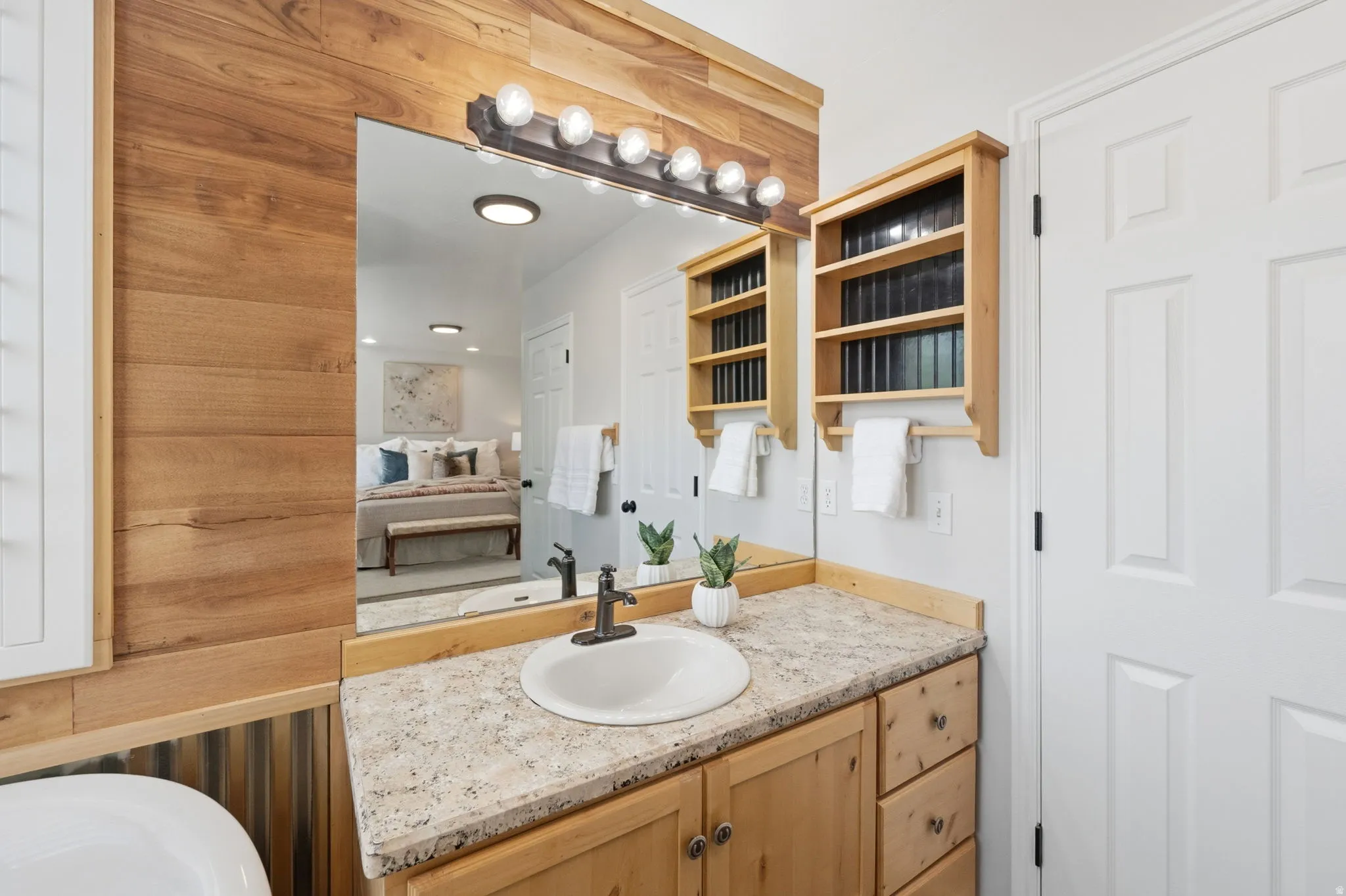 Bathroom vanity with a round undermount sink, granite-style countertop, natural wood cabinetry, and a multi-bulb light fixture
