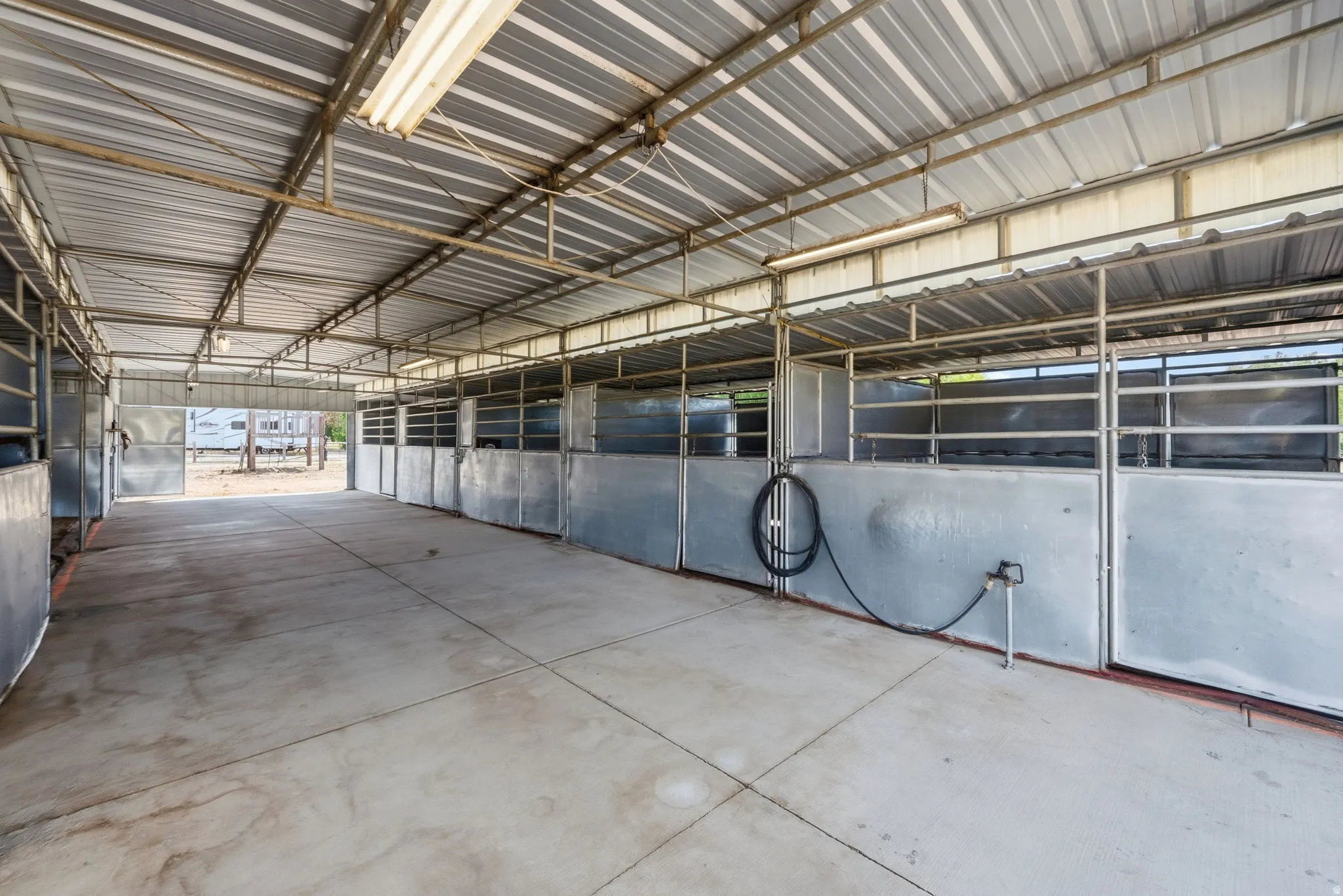 Covered multi-stall structure featuring a corrugated metal roof, concrete flooring, and individual metal stalls