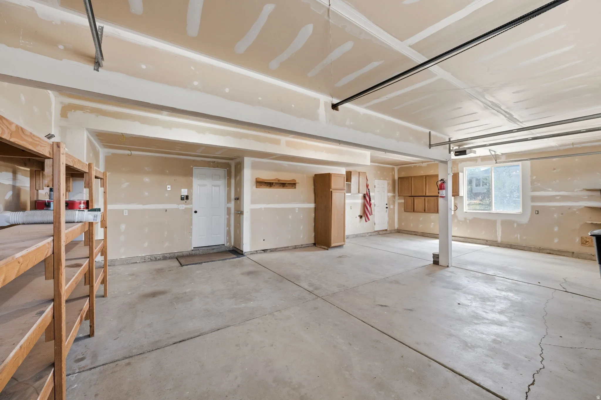 Spacious garage with concrete flooring, multiple built-in storage shelves, interior access door, and a prominent window