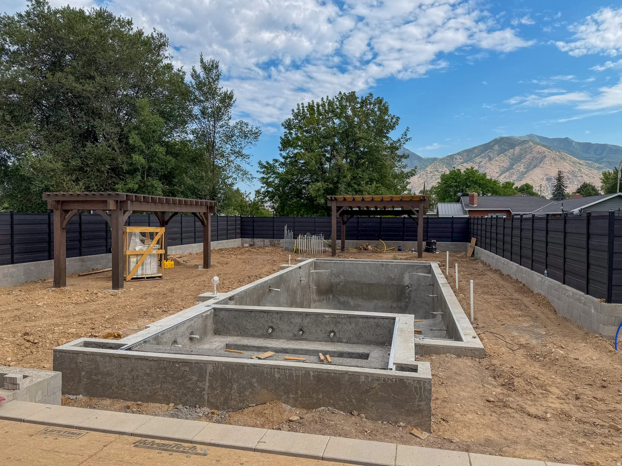 Backyard featuring an in-ground pool and spa shell, two wooden pergolas, and a perimeter fence with a concrete foundation