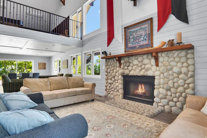 Great room featuring a river rock fireplace with a wood mantle, vaulted ceilings, and a second-story interior balcony with metal railings