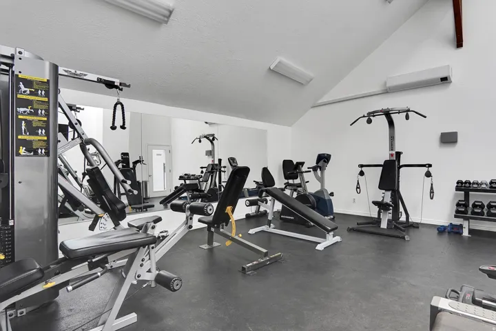 Dedicated fitness area featuring rubber flooring, mirrored wall, and vaulted ceiling