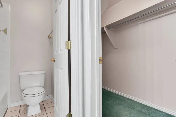 Bathroom with a white toilet, light-toned wall paint, and beige tile flooring