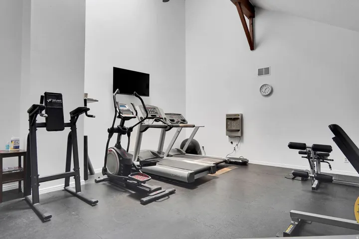 Dedicated fitness area featuring high ceilings, exposed architectural beams, durable rubber flooring, a mounted television, and a built-in water fountain
