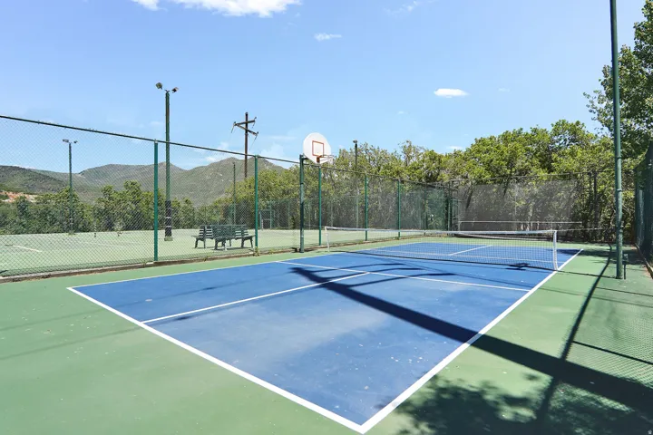 Pickleball court featuring a surface with white boundary lines.  Tennis courts in the background (under repari)