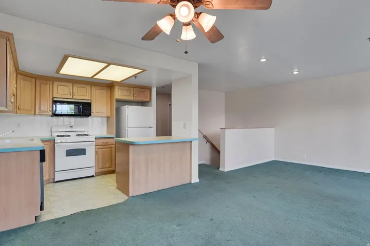 Kitchen featuring natural wood-finish cabinetry, white tile backsplash, a white electric range, and a breakfast bar with light blue countertops