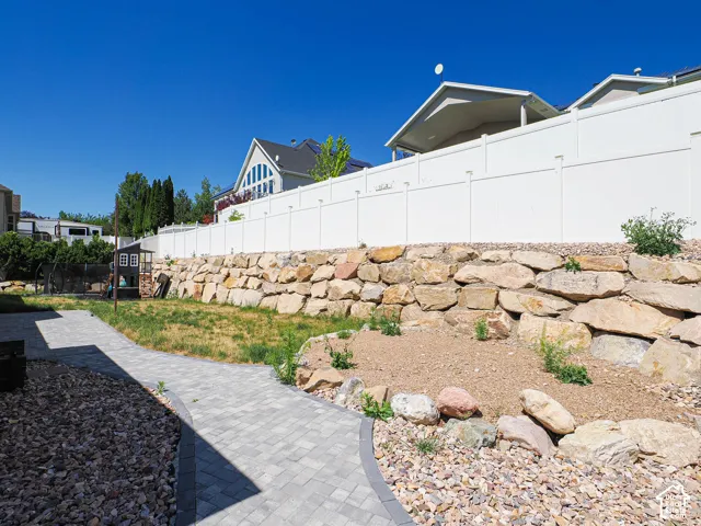 Paver pathway with a gravel border, leading to a retaining rock wall, a level grassy area, and a white privacy fence