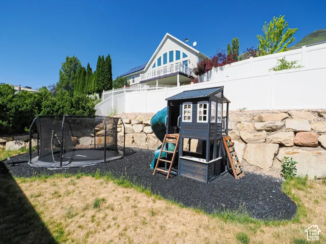 Expansive backyard featuring a rock retaining wall, white privacy fencing, and mature trees