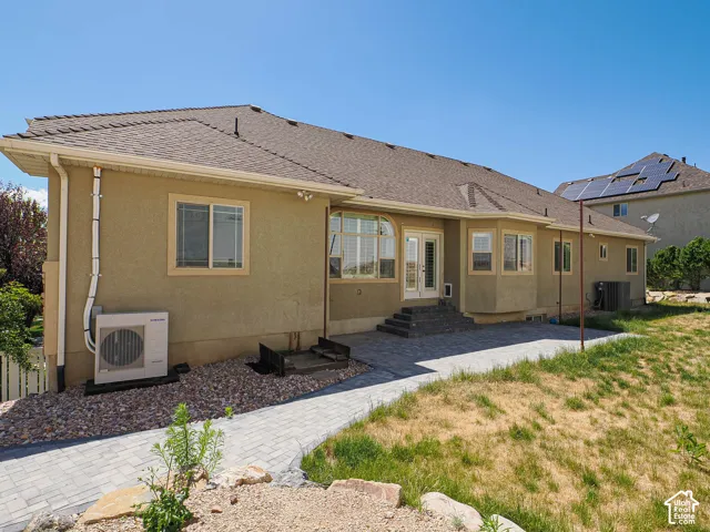 Rear exterior showcasing a neutral stucco finish, a paved patio area, an arched window, and a double glass door entry