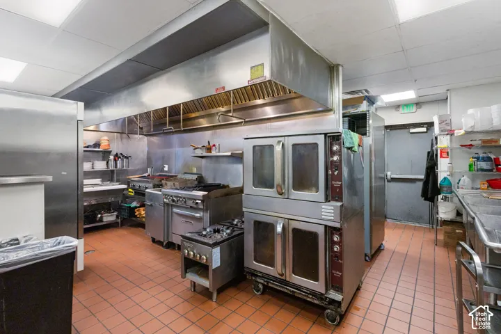Commercial kitchen featuring stainless steel appliances, a large ventilation hood system, dual convection ovens, multiple ranges, and a three-compartment sink
