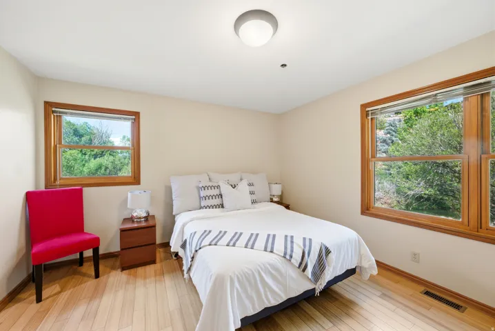 Bedroom featuring light wood-finish flooring, neutral wall tones, and two windows with wood frames