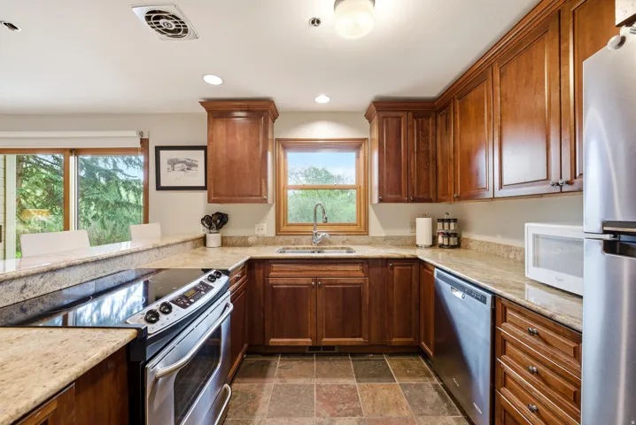 Kitchen featuring warm wood cabinetry, stone countertops, stainless steel appliances, and multi-toned tile flooring