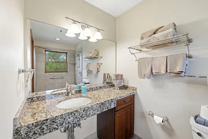Spacious vanity featuring a granite countertop with an undermount sink, ample storage cabinetry, and a large wall-mounted mirror