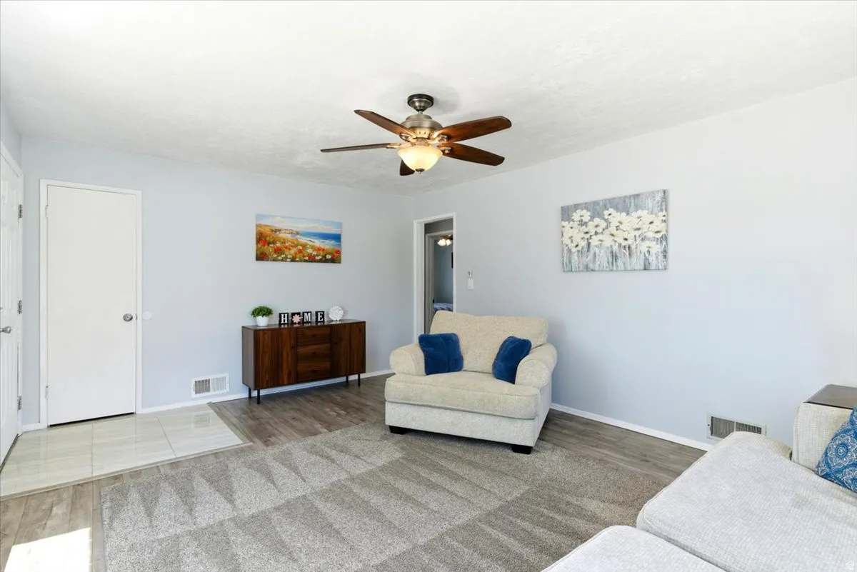 Living area featuring wood-finish flooring, a ceiling fan with integrated lighting, and light gray wall paint