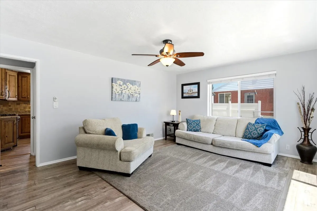 Bright living area featuring wood-finish flooring, light gray wall paint, and a ceiling fan with integrated lighting