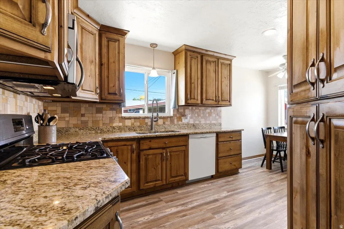 Kitchen featuring wood cabinetry, granite-finish countertops, tile backsplash, laminate flooring, and a stainless steel range hood