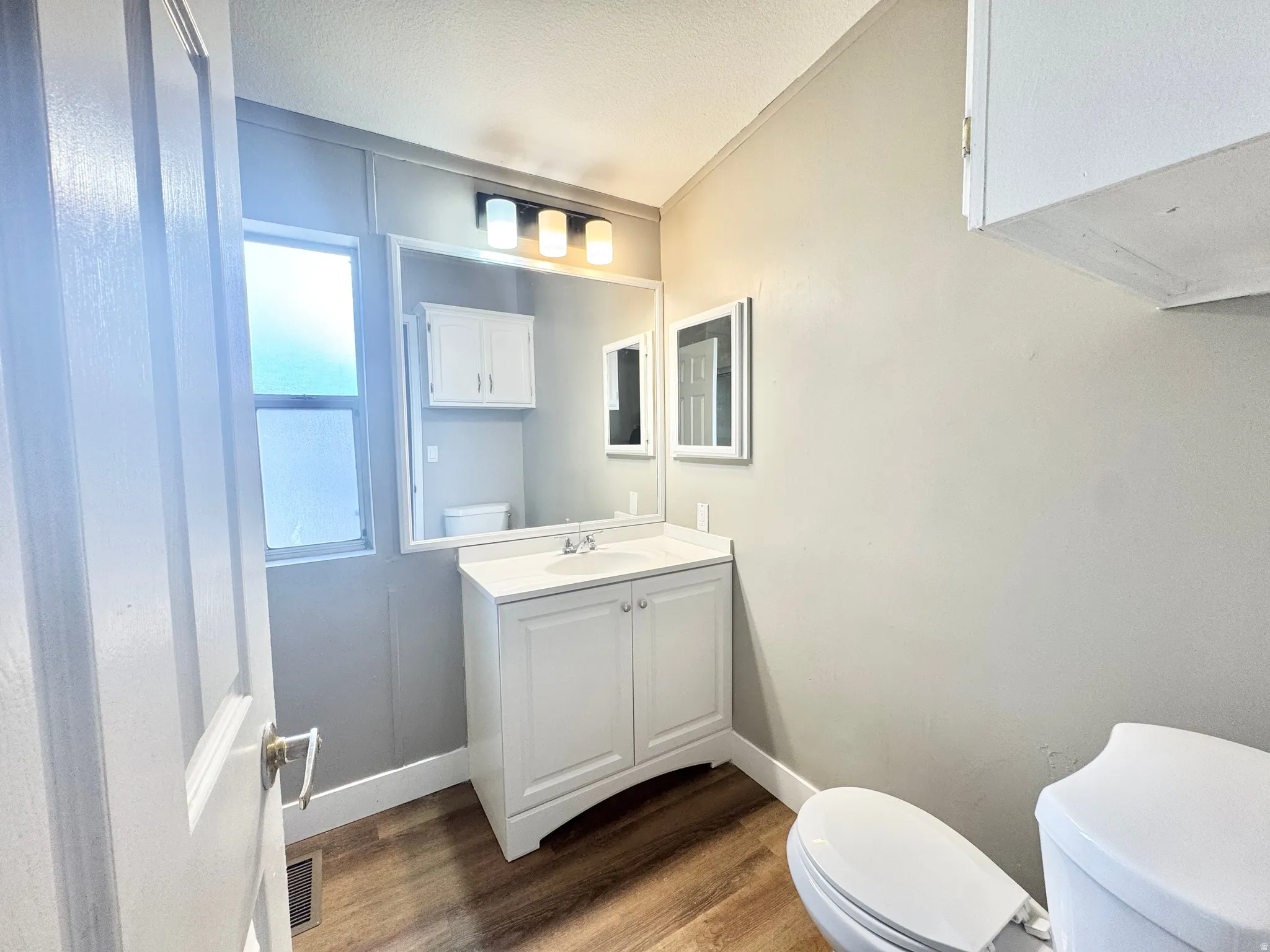 Bathroom featuring a white vanity with integrated sink, a wall-mounted mirror, a three-light vanity fixture, and wood-finish flooring