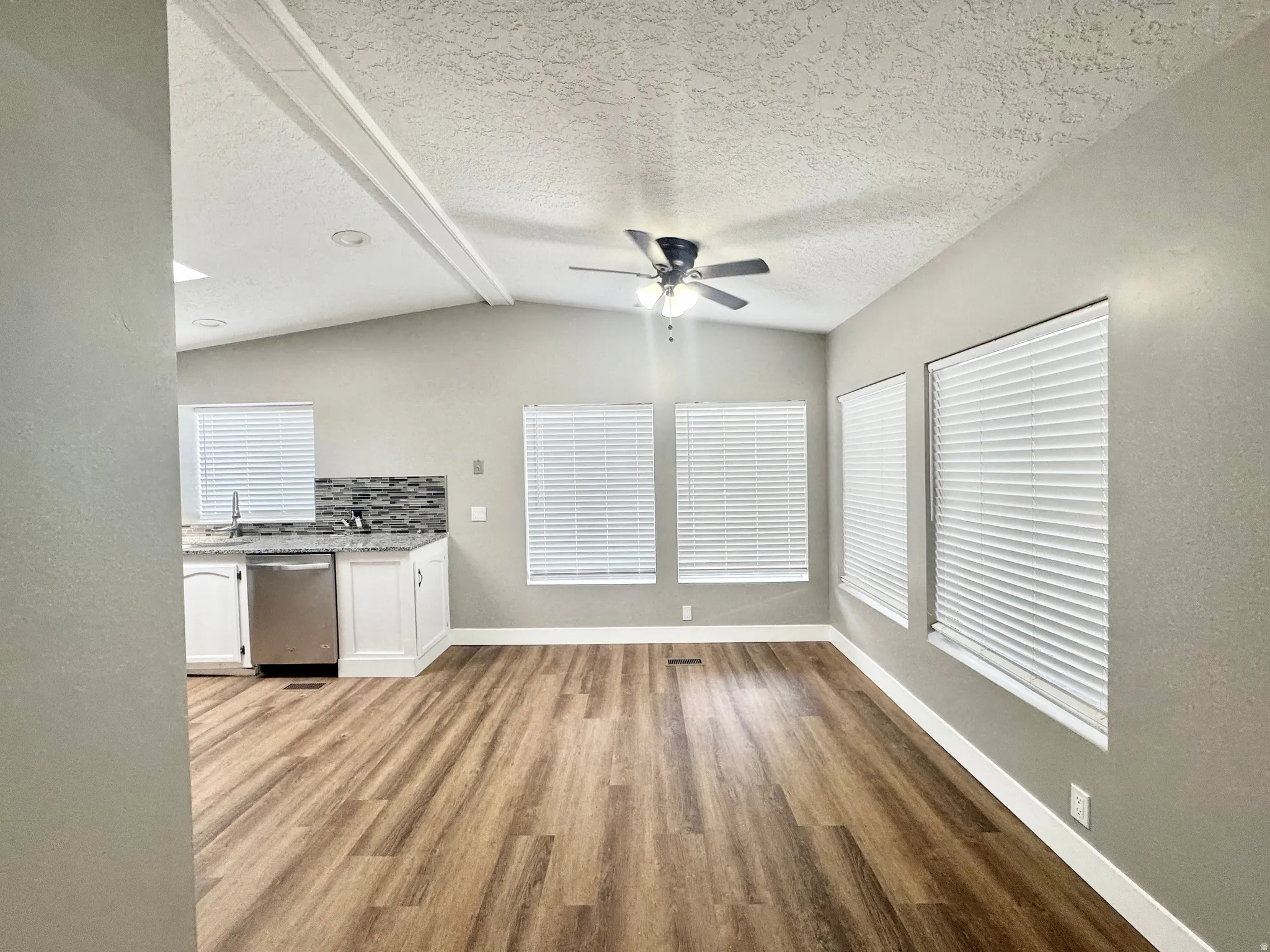 Spacious interior featuring wood-finish flooring, vaulted ceilings with exposed beams, and multiple windows with blinds