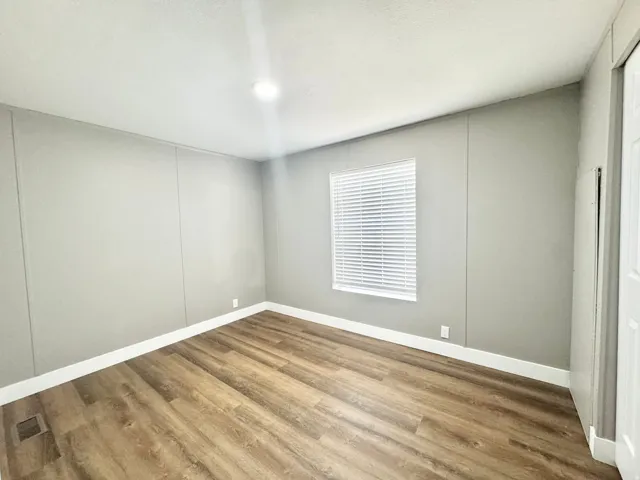 Bright room featuring wood-finish flooring, light gray walls with vertical paneling, white baseboards, and a window with horizontal blinds