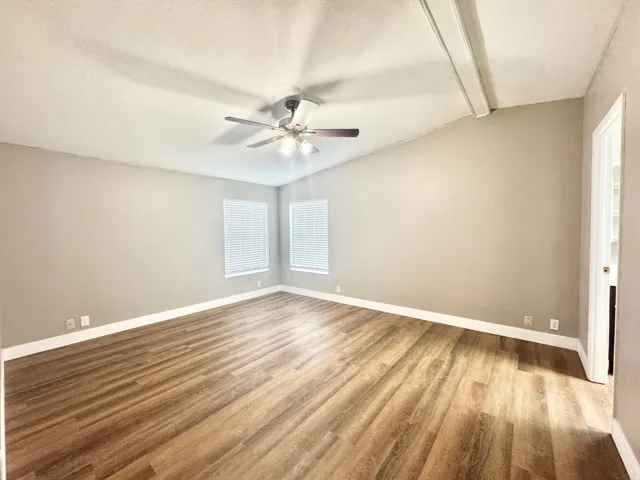 Spacious room featuring wood-finish flooring, vaulted ceiling, and two windows with blinds