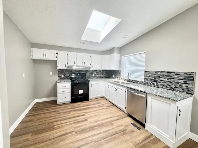 Kitchen featuring wood-finish flooring, white cabinetry, speckled countertops, a mosaic tile backsplash, and a skylight