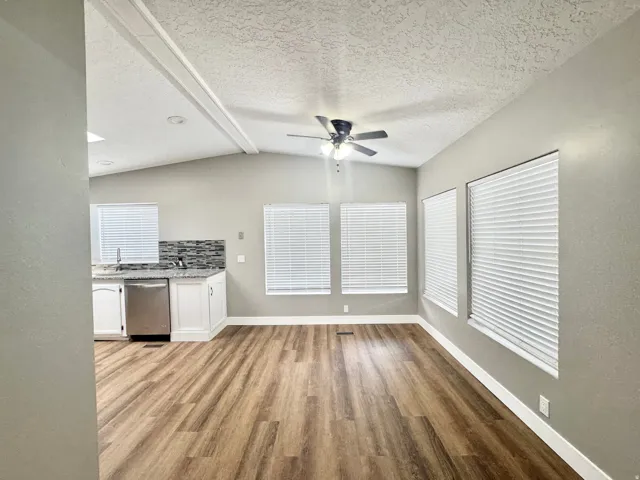 Spacious interior featuring wood-finish flooring, vaulted ceilings with exposed beams, and multiple windows with blinds