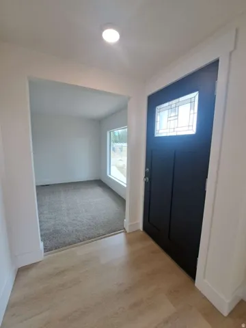 Wood-finish flooring, recessed ceiling lighting, and a dark-paneled door with decorative glass insert