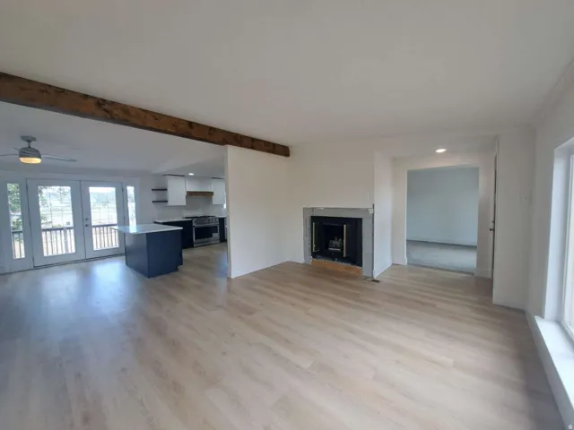 Spacious living area featuring light wood-finish flooring, a contemporary fireplace, and a prominent exposed wood beam