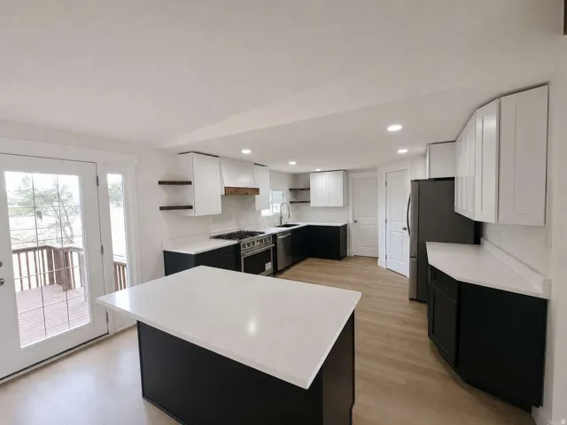 Kitchen featuring white upper cabinetry, dark lower cabinetry, a center island with a white countertop, stainless steel appliances, and light wood-finish flooring