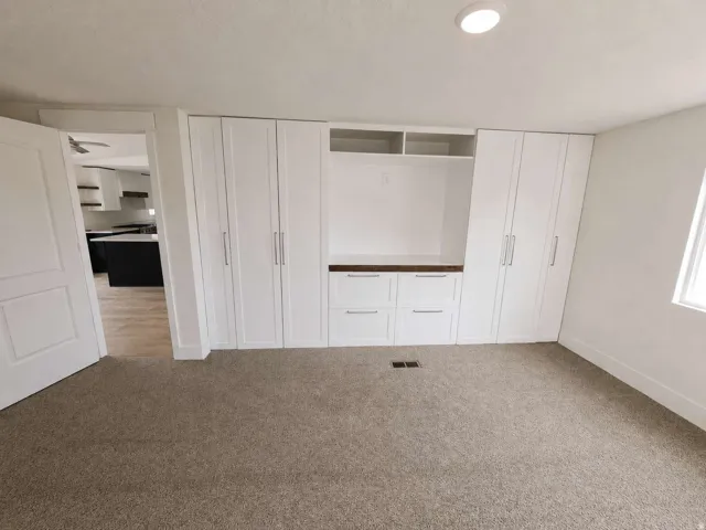 Built-in white cabinetry with chrome hardware, integrated shelving, wood-finish countertop, and plush carpet flooring