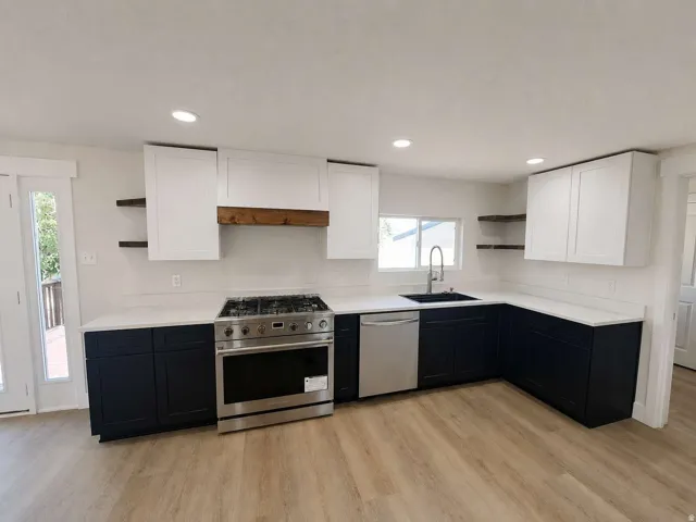 Kitchen featuring stainless steel appliances, wood-finish flooring, two-tone cabinetry, recessed lighting, and a black sink