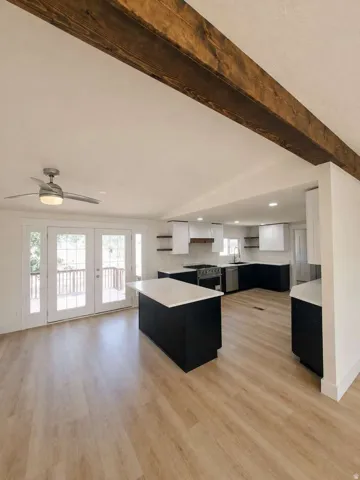 Open-concept kitchen and living area featuring a large wood-finish beam, light wood-finish flooring, and a modern ceiling fan