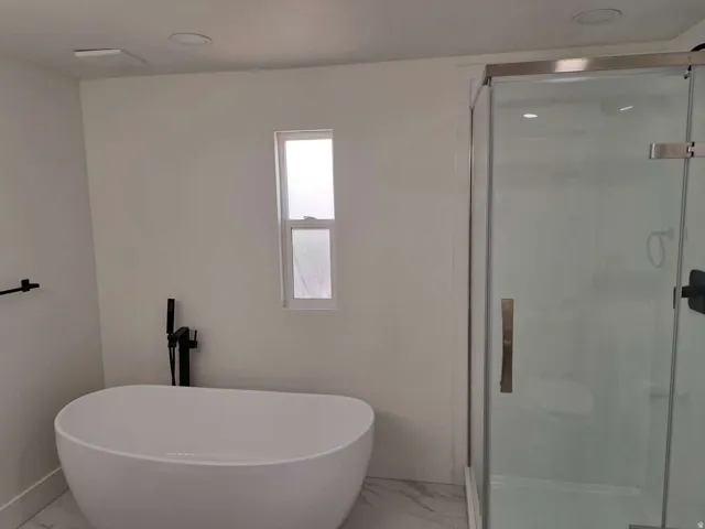 Freestanding soaking tub with a floor-mounted matte black faucet, glass-enclosed shower, and recessed lighting