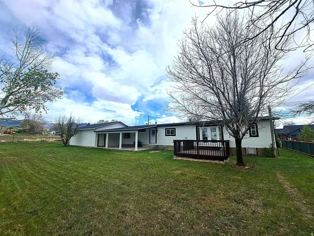 Expansive green lawn with a covered patio, dark wood-finish deck, and white exterior siding