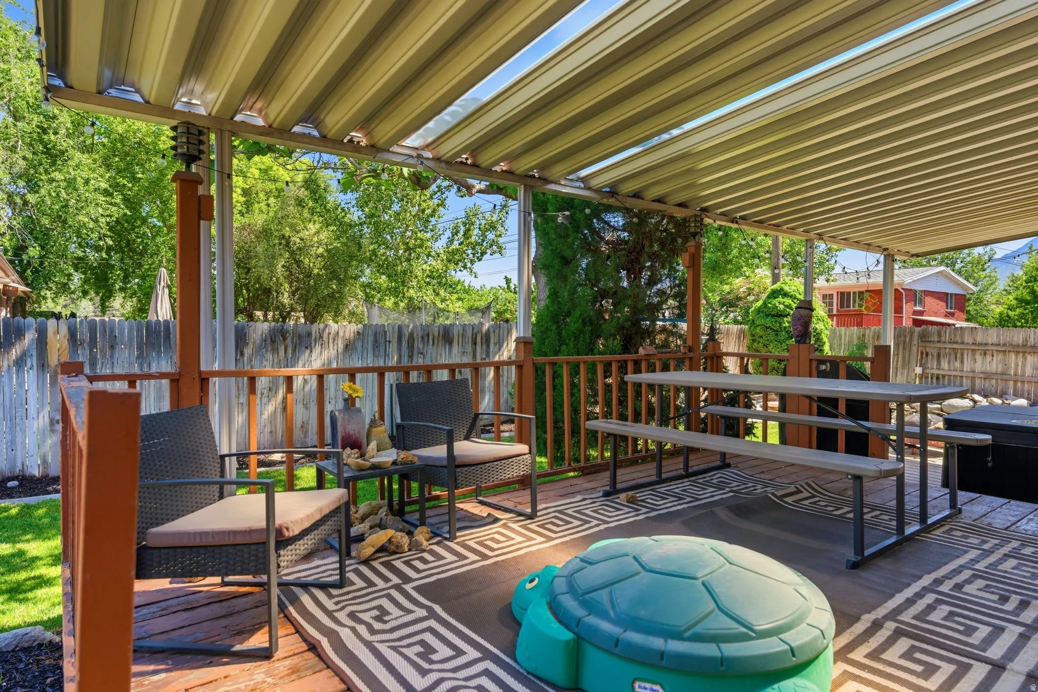 Expansive wood deck featuring a covered patio with a slatted roof, providing overhead coverage