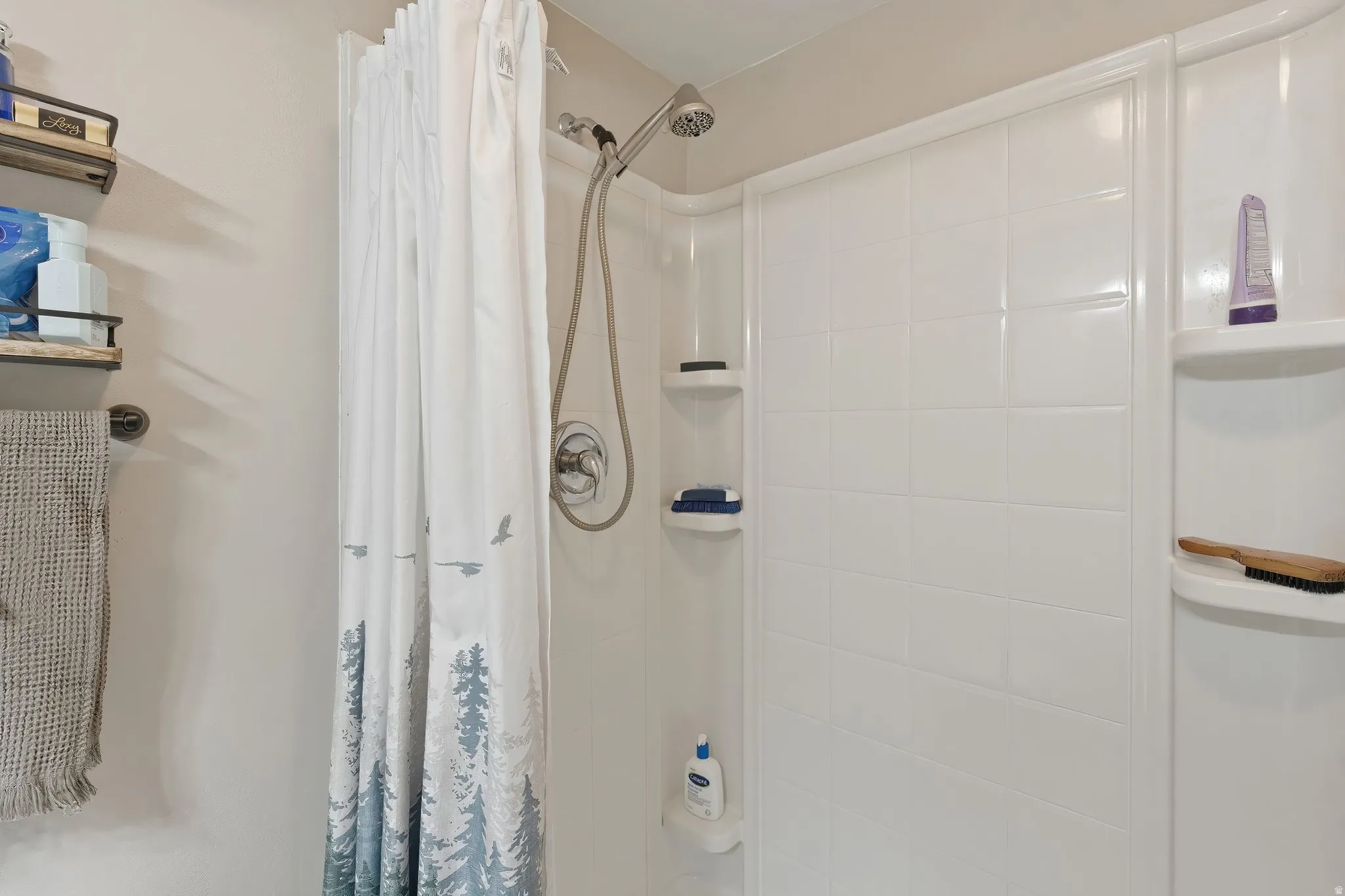 White shower stall featuring an integrated shelving system and a chrome shower head with handheld attachment